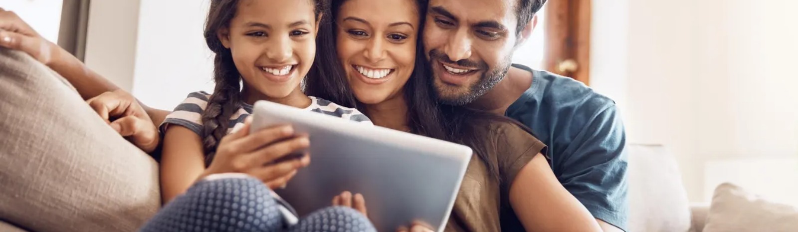 A family of three sitting on a couch looking at a tablet.