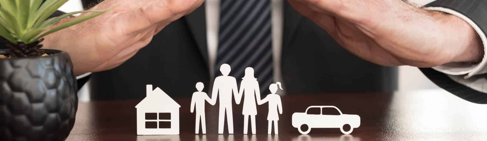 two hands over a paper cuts of a house, family of four and a car